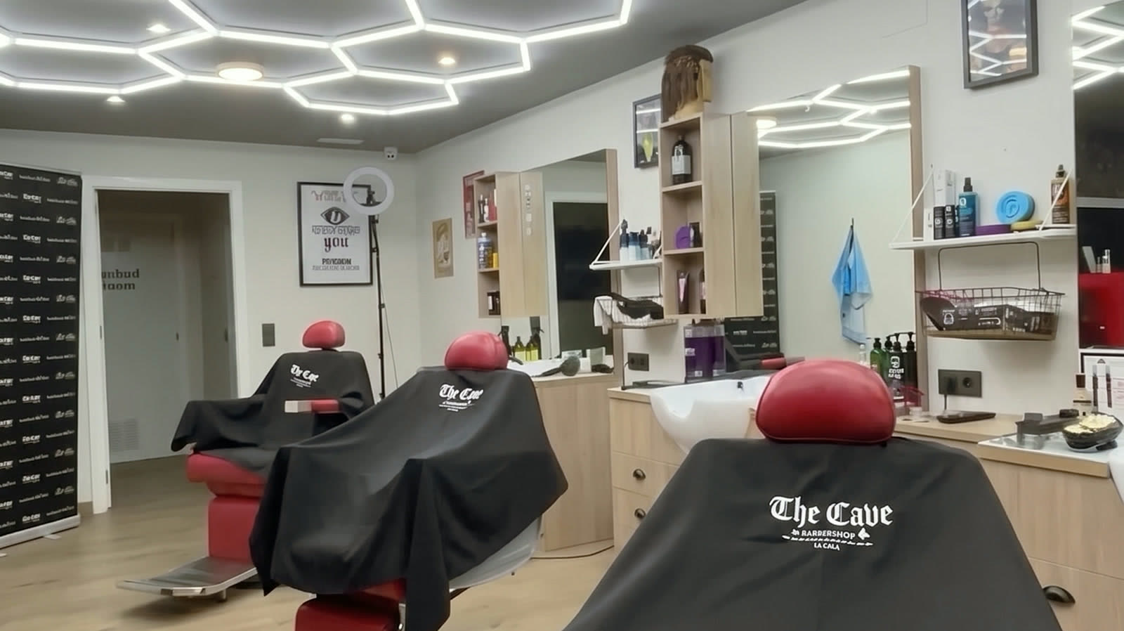 Inside The Cave barbershop in La Cala de Mijas: red barber chairs, branded black capes and the hexagonal LED ceiling