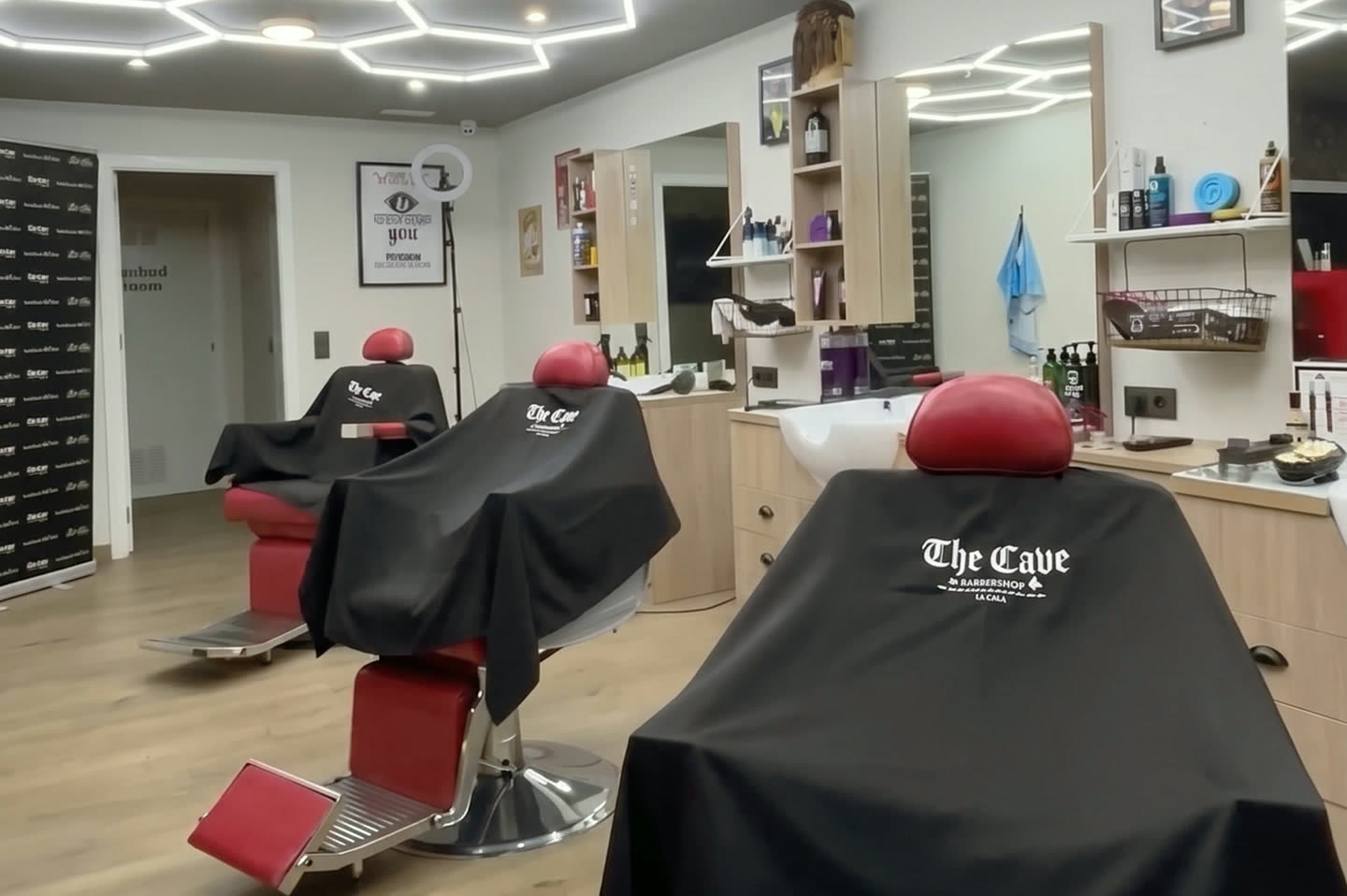 Red leather barber chairs and branded capes under the hexagonal LED ceiling at The Cave